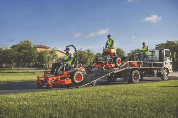 Professionals driving Kubota mowers off the back of trailer
