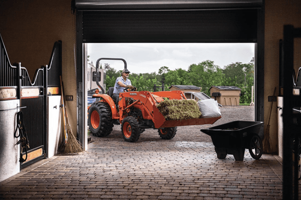 Man hauling hay stacks in tractor's bucket