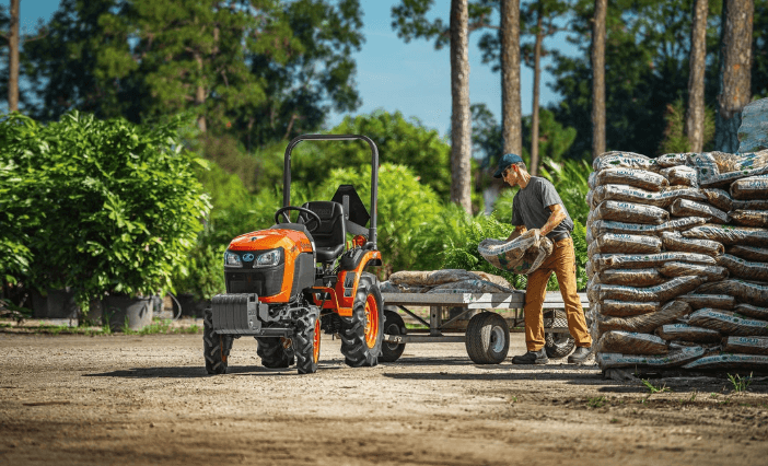 Kubota B2401 Narrow tractor hauling a trailer of bagged soil at a plant nursery