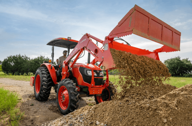 Kubota M6060 tractor with front loader dumping dirt on a ranch