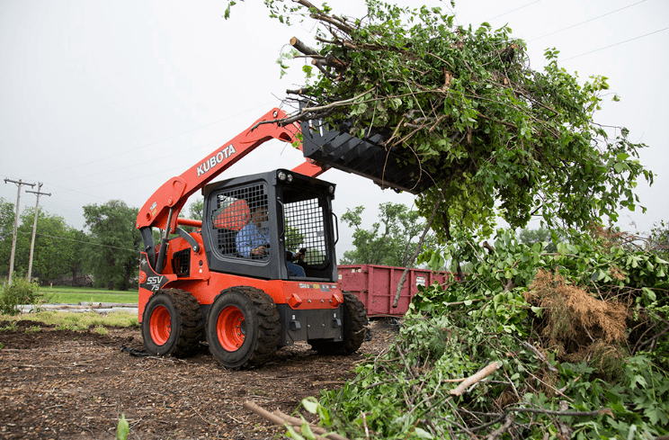 Kubota SSV75 skid steer loading tree branches and debris into a trailer